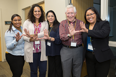 This is an image of Dr. West and a few of his students. They are using their hands to gesture the letter "U."